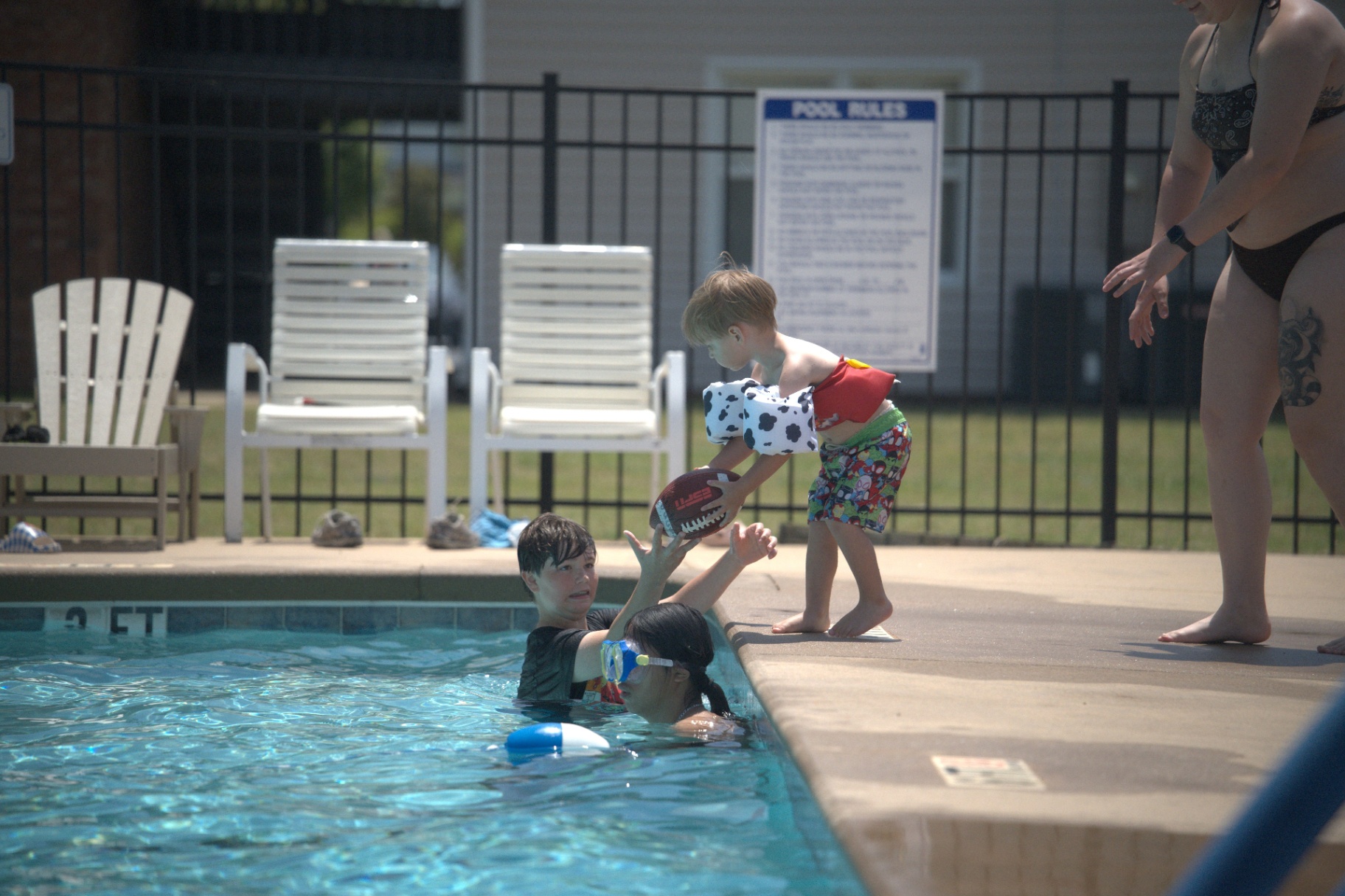 Kids passing a football at the pool's edge